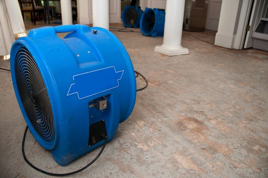 Blue industrial air mover drying a water-damaged floor in a home interior